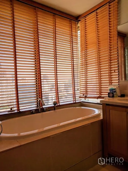 Condominium for rent - Bathroom with corner bathtub beside wraparound windows fitted with wooden blinds.