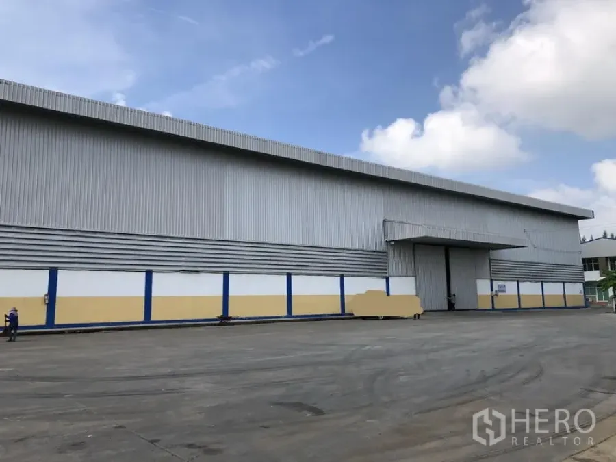Warehouse for rent in Phra Nakhon Si Ayutthaya - Side elevation of a modern warehouse with blue and yellow base panels and a loading bay.