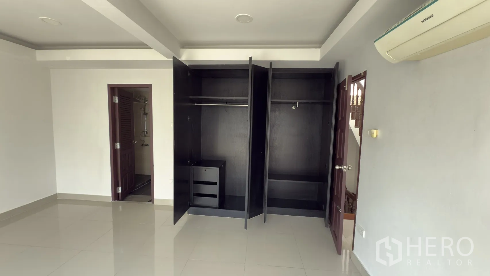 Townhouse for rent in Watthana, Bangkok - Spacious bedroom with two open wardrobes, glossy flooring, and an entrance to the ensuite.