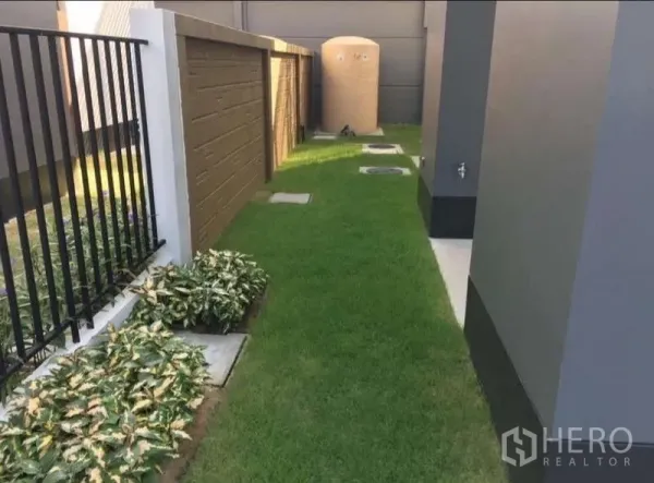 Detached House for rent in Bang Kapi, Bangkok - Narrow side yard with green grass, utility tank and planted borders along the fences.