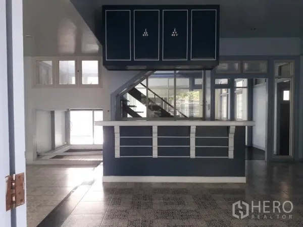 Detached House for rent in Watthana, Bangkok - Open-plan living area with a built-in counter and staircase beneath dark cabinetry.
