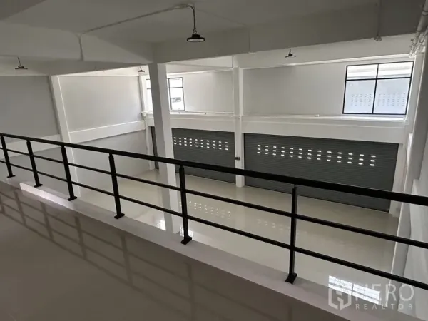 Warehouse for rent in Bang Phli, Samut Prakan - Mezzanine walkway with safety railing overlooking the loading area and roller shutters below.