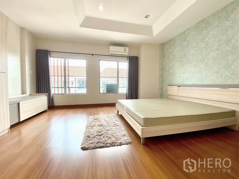 Townhouse for rent in Prawet, Bangkok - Spacious master bedroom with wood flooring, feature wall, large windows and air conditioner.