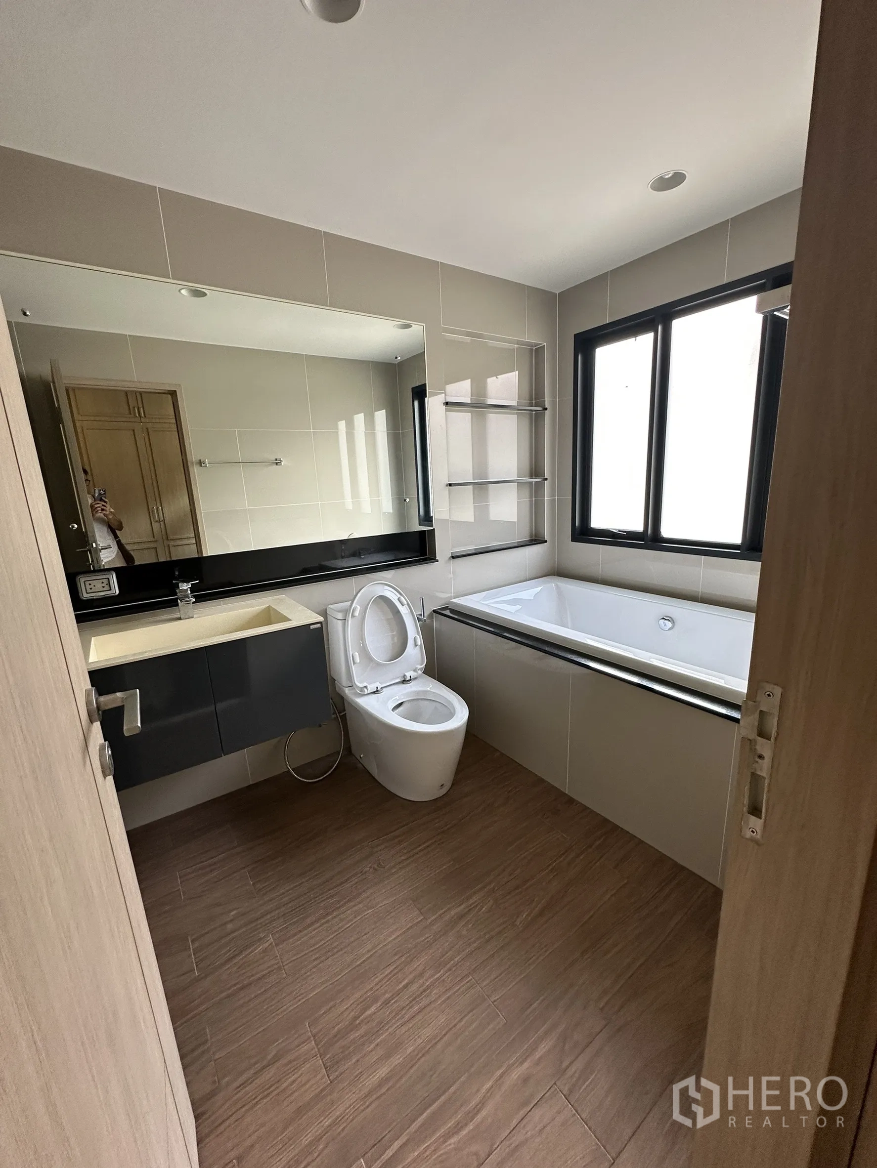 Detached House for sale in Lam Luk Ka, Pathum Thani - Bathroom with bathtub, vanity and wood-look floor tiles next to a window.