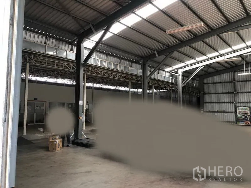 Warehouse for rent in Pak Kret, Nonthaburi - Interior view showing steel columns, skylights, loading ramp and partitioned admin area.