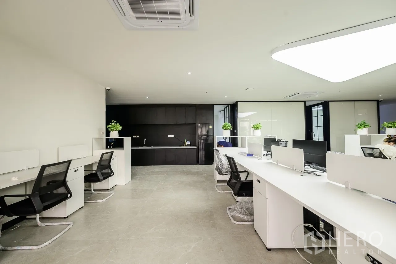 Office Space for rent or sale in Huai Khwang, Bangkok - Open-plan office with long bench desks facing a dark kitchenette.