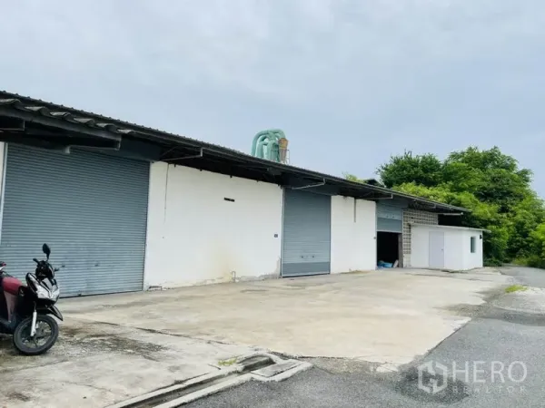工厂 出租在Bang Pakong, Chachoengsao - 工厂外立面设多处卷帘门，前方大进深硬地，侧边绿化带。