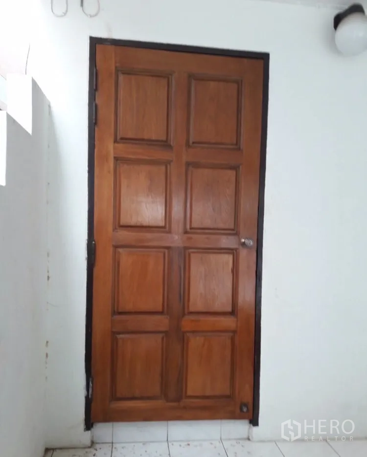 Townhouse for rent in Watthana, Bangkok - Solid wooden panel door in a white-walled corridor.