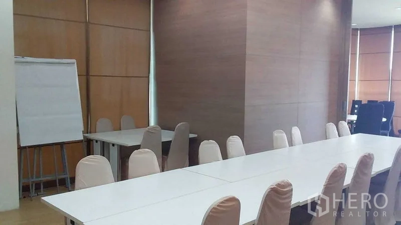 Office Space for rent in Phra Khanong, Bangkok - Training room setup with joined tables, a flip chart, wood-panel walls, and natural daylight.