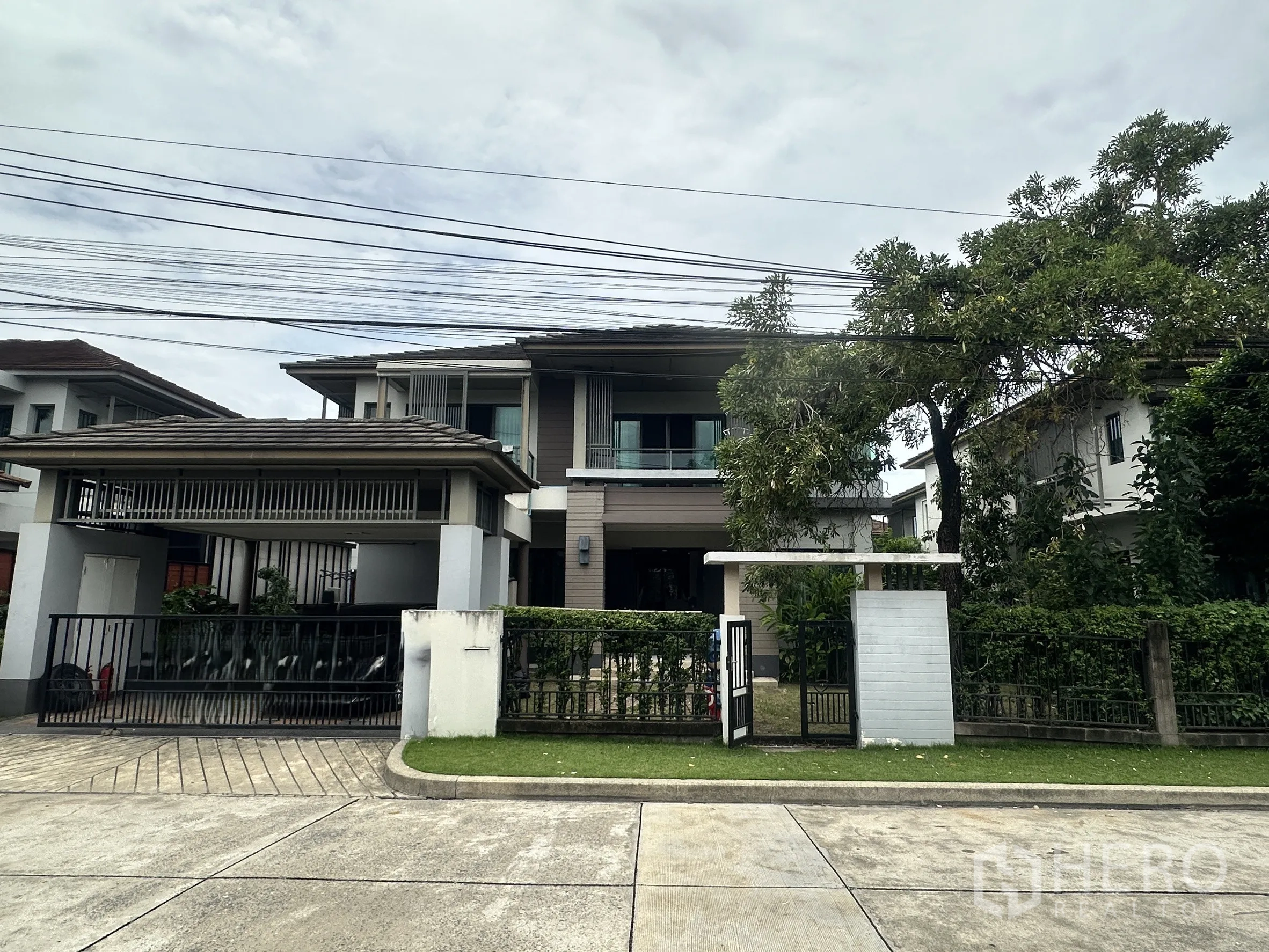 独栋房屋 for sale in Pak Kret, Nonthaburi - 两层独栋别墅外观，带大门、车道与绿树。