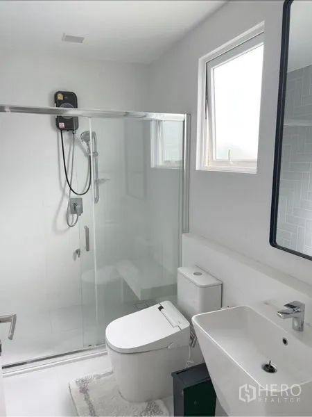 Detached House for rent or sale in Prawet, Bangkok - White bathroom with glass shower, window and contemporary fixtures.