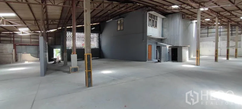 Warehouse for rent in Phra Khanong, Bangkok - Wide storage hall featuring steel columns, truss roof lighting, and a central attached office block.