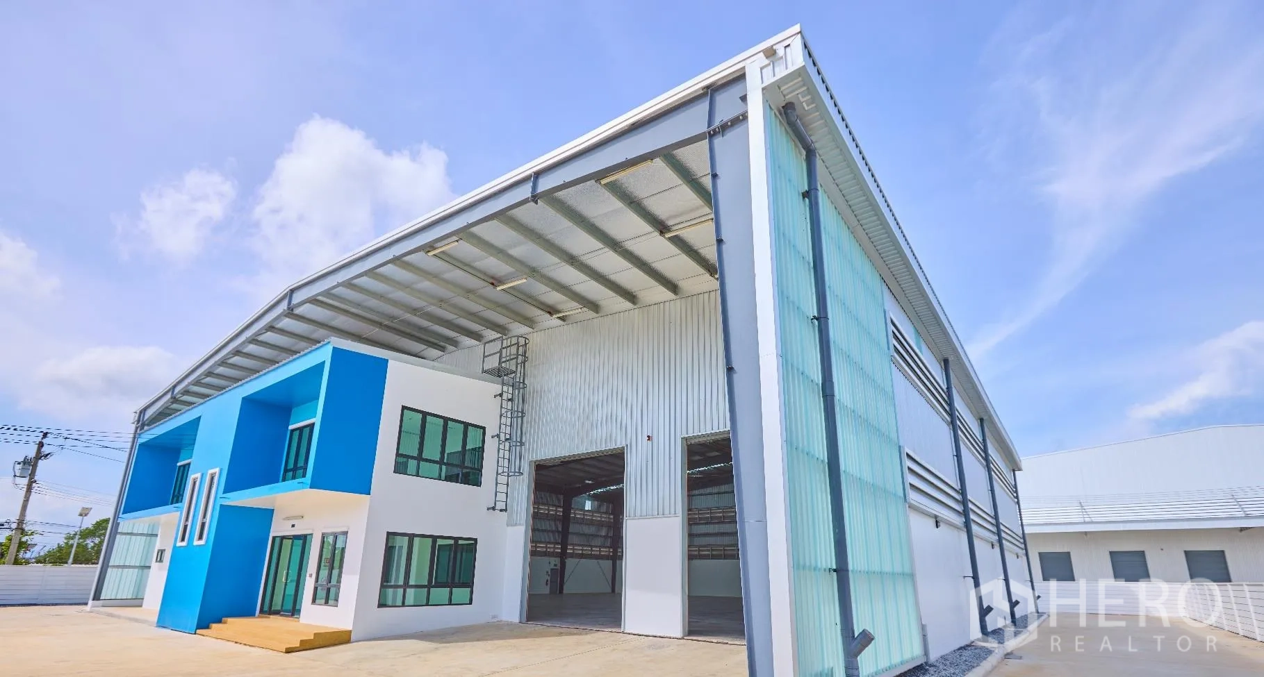 工厂 for rent in Bang Sao Thong, Samut Prakan - 蓝白配色的工厂外观，双电动卷帘高门与宽阔混凝土场地。