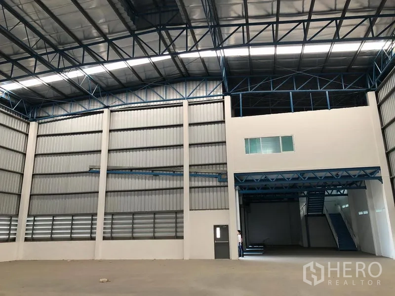 货栈 出租在Lat Krabang, Bangkok - 仓库内部一角，设夹层办公室、宽幅卷帘门与蓝色钢结构。