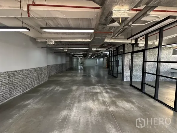 Office Space for rent - Long office corridor with black-framed glass partitions and brick accent walls.