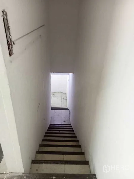 零售空间 出租在Watthana, Bangkok - 店铺内通往下层的楼梯，白色墙面与瓷砖台阶。