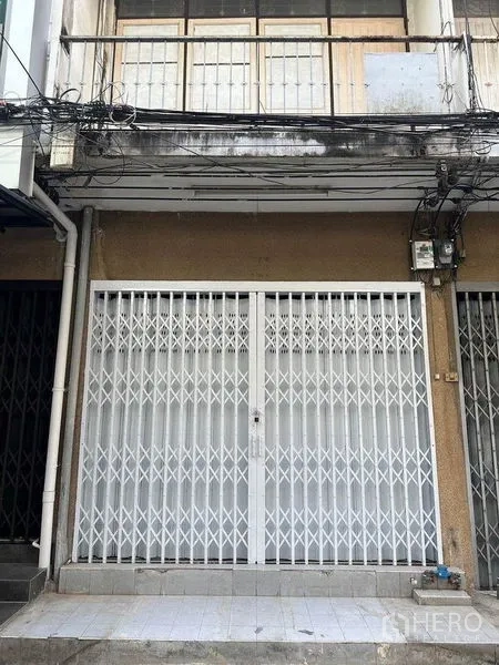 Shophouse for rent in Khlong Toei, Bangkok - Street-facing shophouse facade with white folding steel security gate and balcony above.