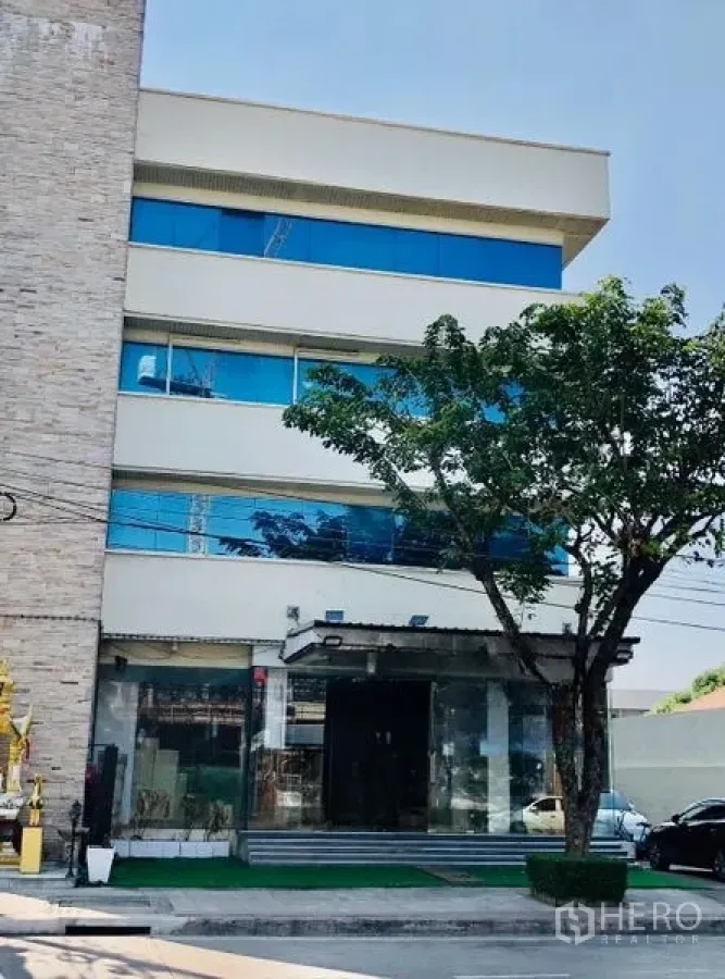 Shophouse for rent in Lat Phrao, Bangkok - Street view of the shophouse exterior featuring mirrored windows, front steps and a shaded tree.