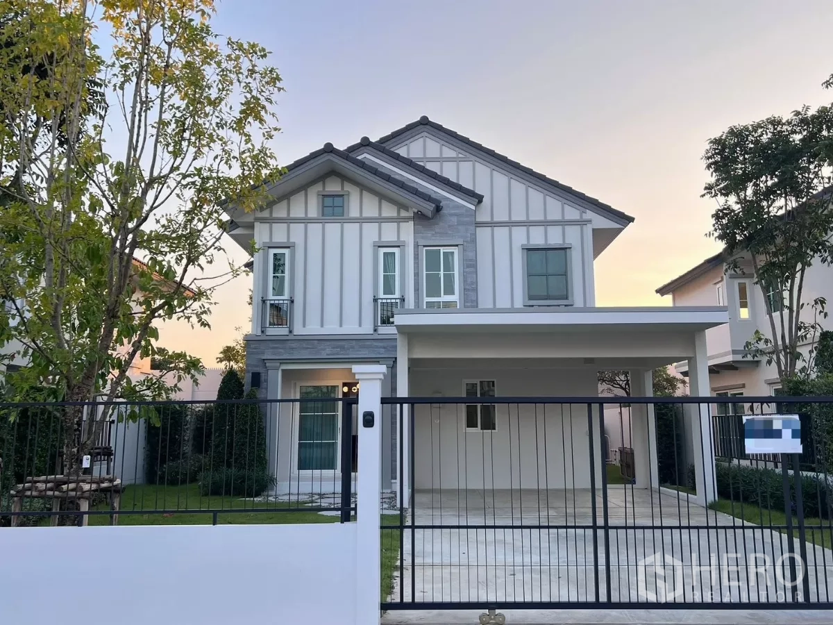 Detached House for rent in Bang Phli, Samut Prakan - Front elevation of a modern two-storey detached house with gated driveway and lawn at sunset.