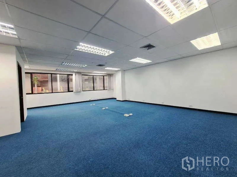 Office Space for rent in Khlong Toei, Bangkok - Large office area with fluorescent lighting, curtains, and floor power outlets for workstations.
