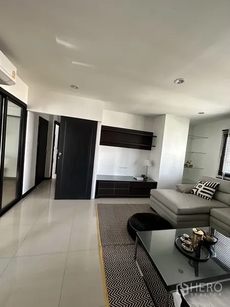 Condominium for rent in Khlong Toei, Bangkok - Living area facing built-in shelving and hallway with glossy tiled floors.