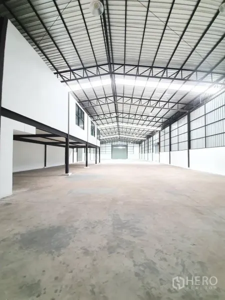 Warehouse for rent in Bang Khen, Bangkok - Spacious warehouse interior showing high steel truss ceiling, polished concrete floor and mezzanine offices with windows.