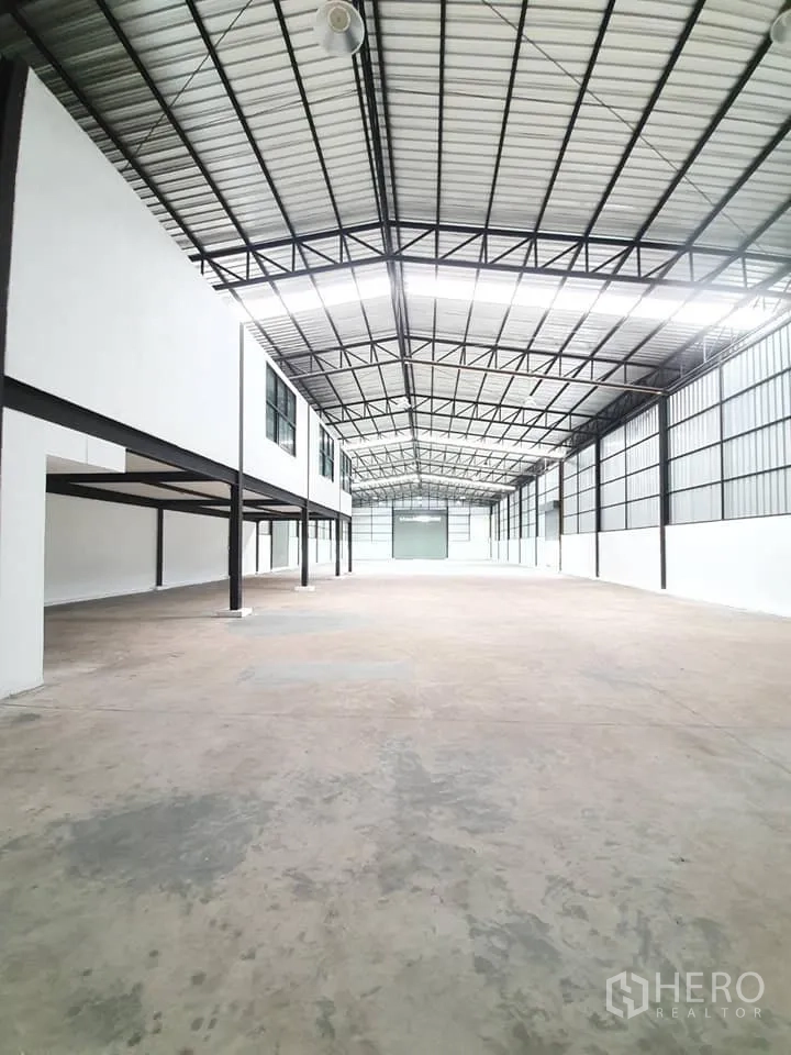 Warehouse for rent in Bang Khen, Bangkok - Spacious warehouse interior showing high steel truss ceiling, polished concrete floor and mezzanine offices with windows.