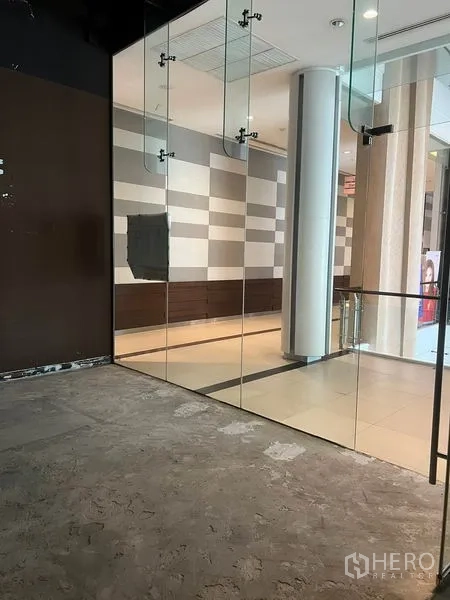 Retail Space for rent in Watthana, Bangkok - Small retail unit with floor-to-ceiling glass frontage and concrete floor along a modern mall corridor in Watthana, Bangkok.