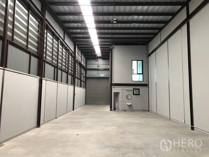 Warehouse for rent in Bang Phli, Samut Prakan - Warehouse hall facing roller shutter with built-in restroom and high ceiling lighting.