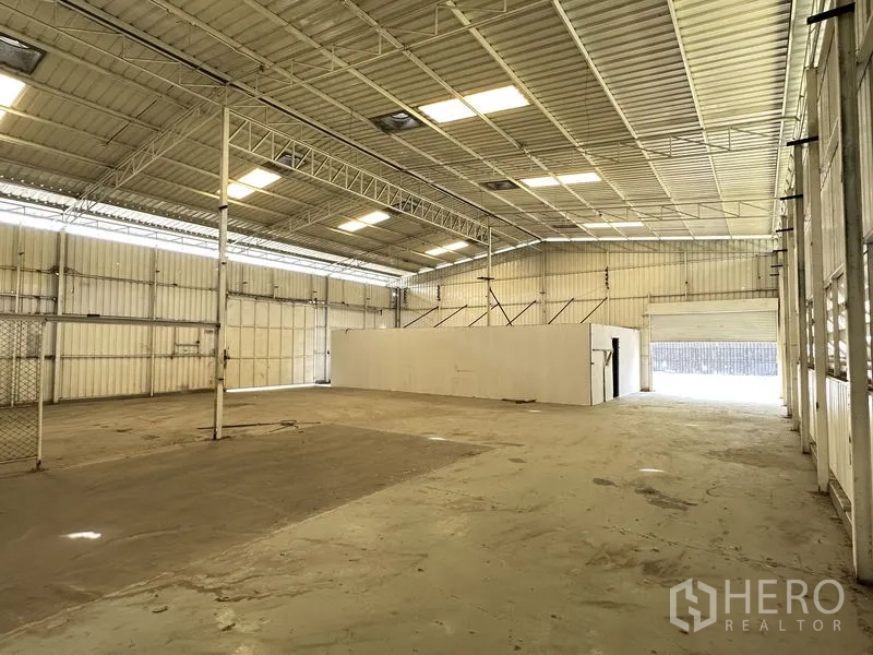 Warehouse for rent in Min Buri, Bangkok - Open-plan warehouse interior with roller door access, bright skylights, and a central partition room.