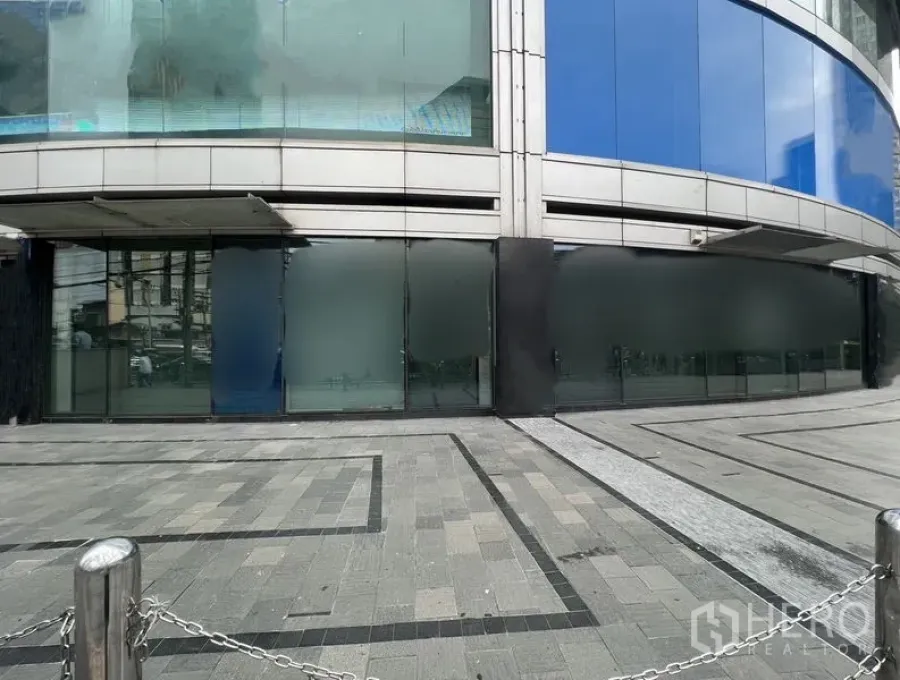 Retail Space for rent - Street-level view of large shopfront windows and a broad stone plaza with stainless-steel bollards.