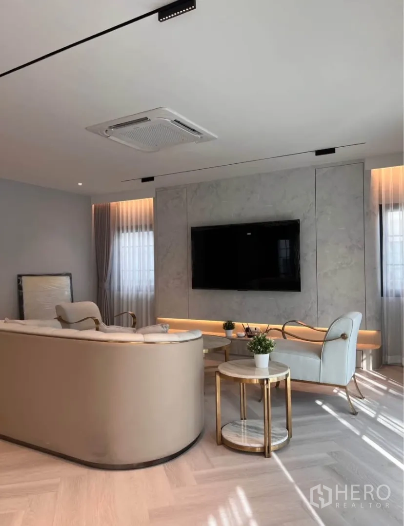 Detached House for rent in Bang Phli, Samut Prakan - Living room feature wall with mounted TV, curved sofa, round side tables and recessed lighting.