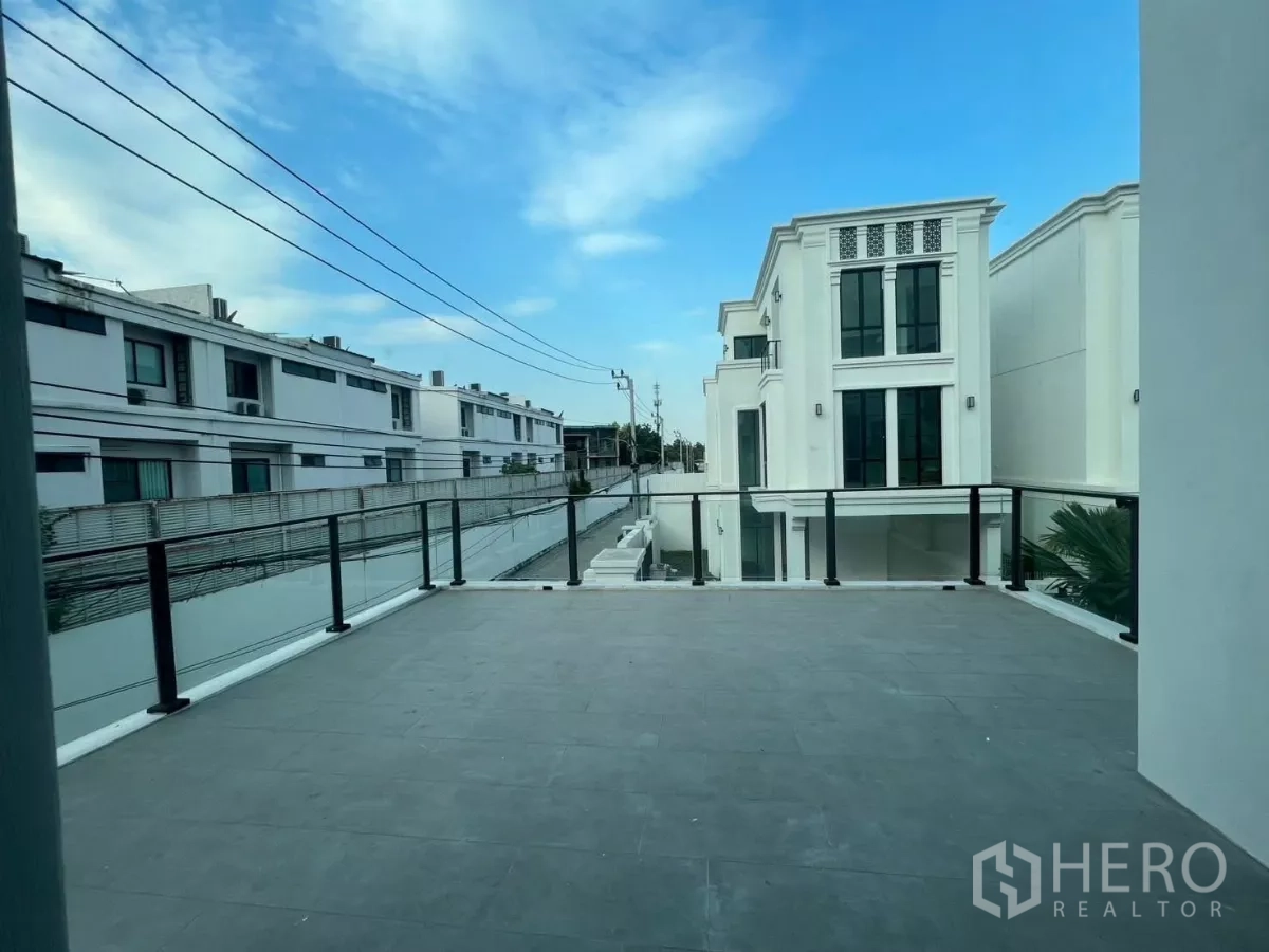 Detached House for rent in Lat Phrao, Bangkok - Expansive terrace balcony with glass railing and views over a modern housing estate under blue sky.