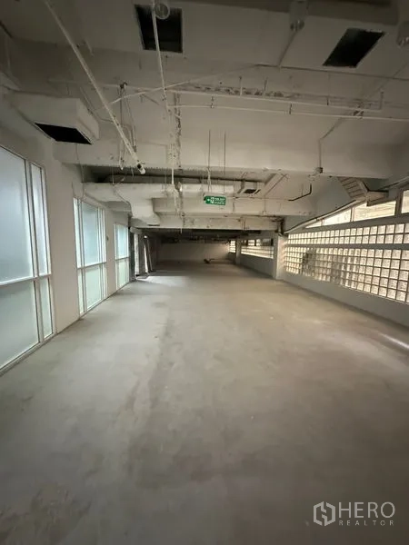 Retail Space for rent - Unfurnished 125 sqm retail shell with industrial-style ceiling, exit signage, and soft natural light from glass blocks and windows.