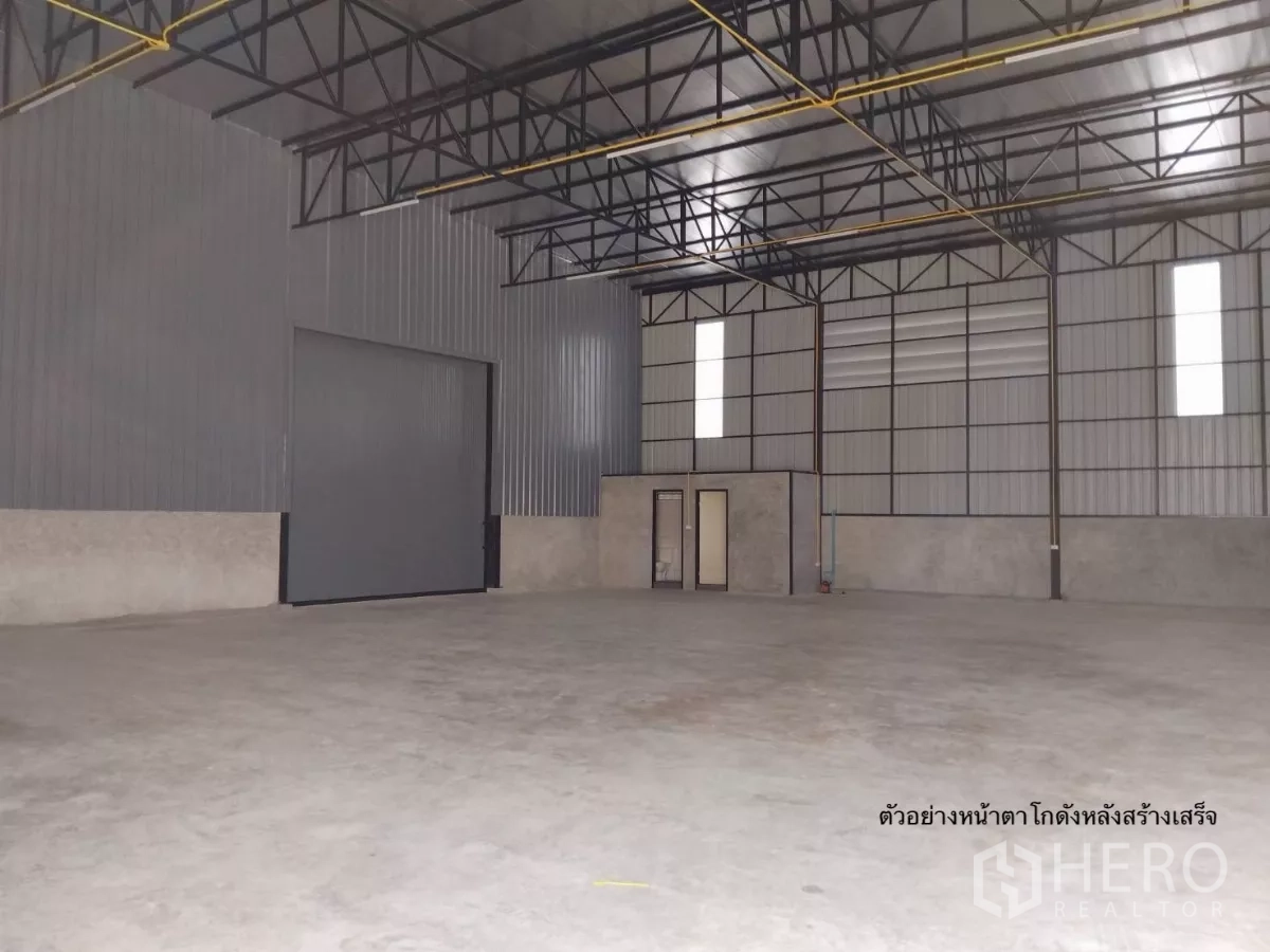Warehouse for rent in Bang Kapi, Bangkok - Spacious warehouse interior with high ceiling, steel trusses, concrete floor, a roller shutter and a small office.