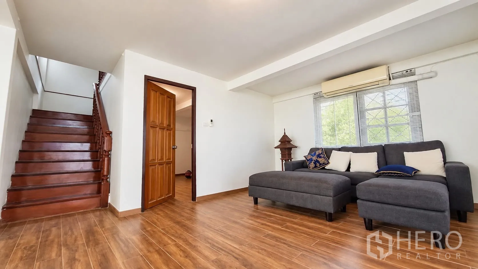 Detached House for rent in Khlong Toei, Bangkok - Living room with gray sectional sofa, wood-look floor, and staircase nearby.