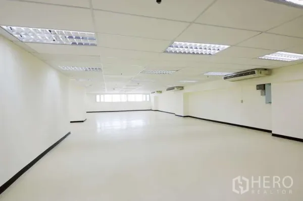 Office Space for rent - Large open-plan office interior with drop ceiling, fluorescent lights, air conditioners, and window line.