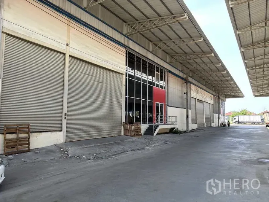 Factory for rent in Bang Phli, Samut Prakan - Covered loading bays with multiple roller shutter doors along a wide concrete driveway at a modern factory in Bang Phli.
