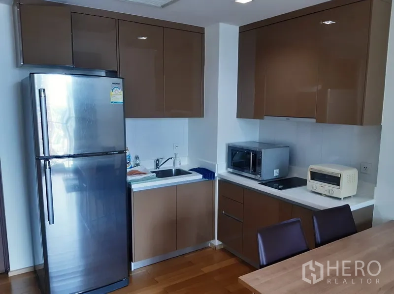 Condominium for sale in Khlong Toei, Bangkok - Modern condo kitchen with stainless fridge, sleek brown cabinets, microwave and cooktop.