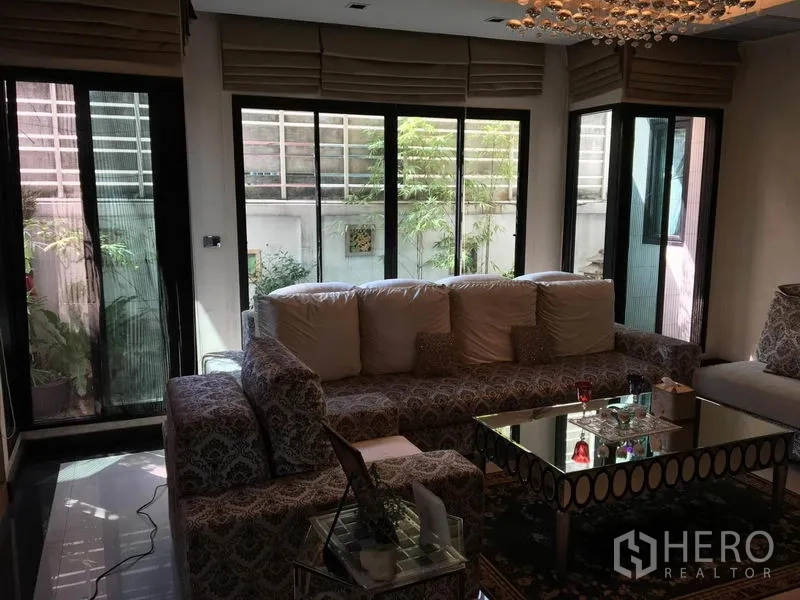 独立式住宅 出租在Khlong Toei, Bangkok - 客厅另一视角，转角沙发、镜面茶几与宽幅推拉窗。