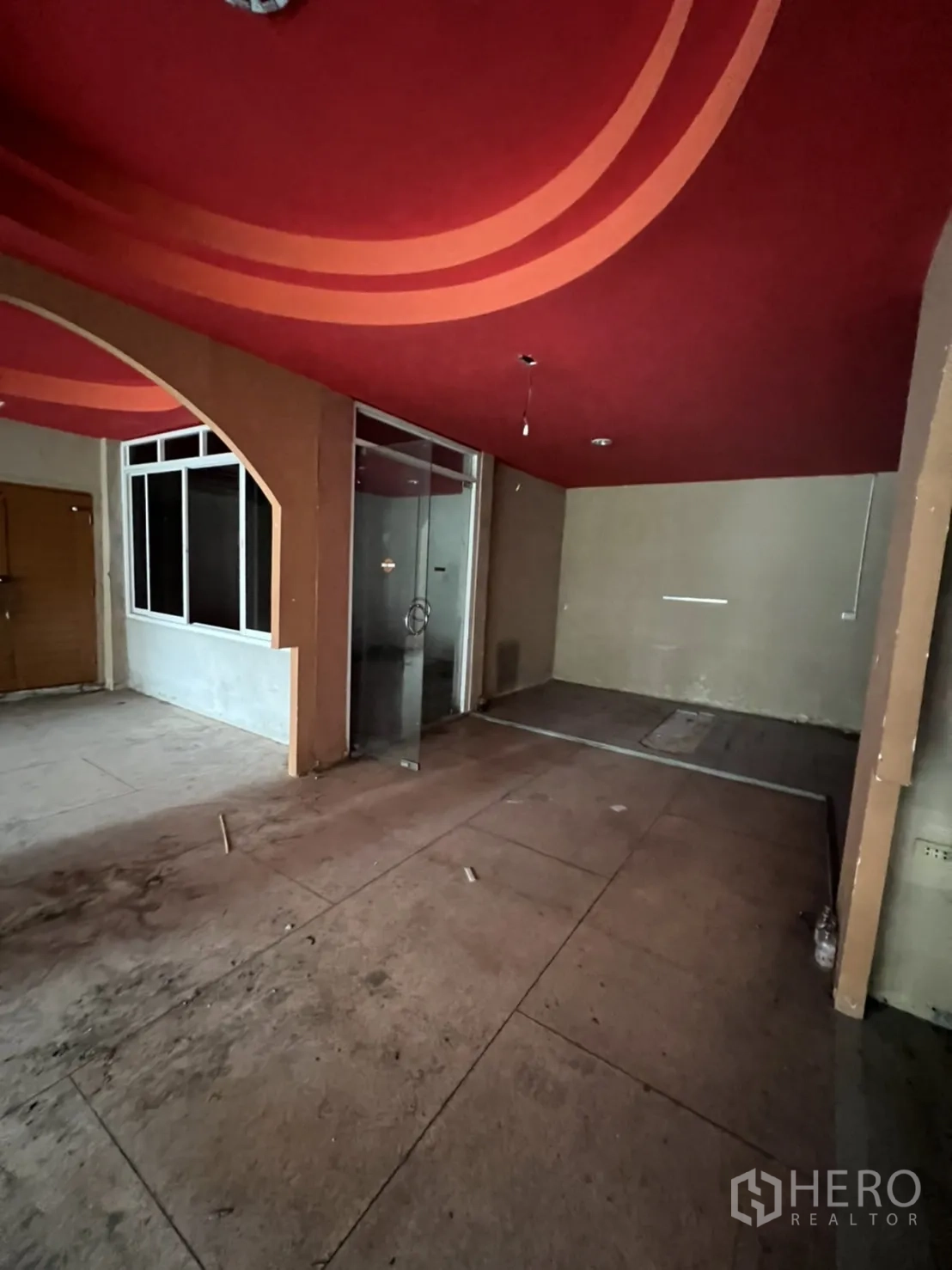 Shophouse for rent in Watthana, Bangkok - Ground-floor interior with red curved ceiling, glass partition and concrete floor ready for fit-out.