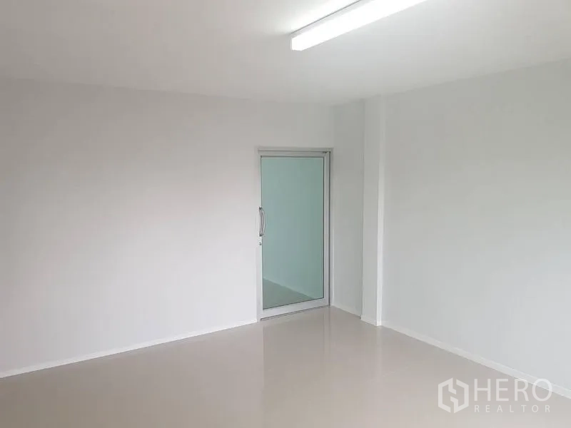 Shophouse for rent or sale in Lat Phrao, Bangkok - Bright minimalist room with smooth floors and a glass door to an inner space.