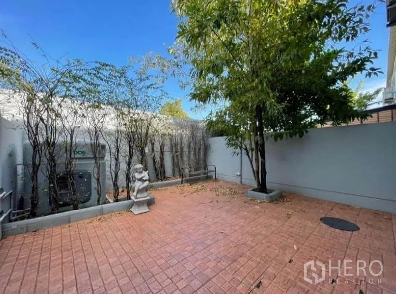 Townhouse for rent in Prawet, Bangkok - Walled patio with red tile paving, a tree, and hedge screening