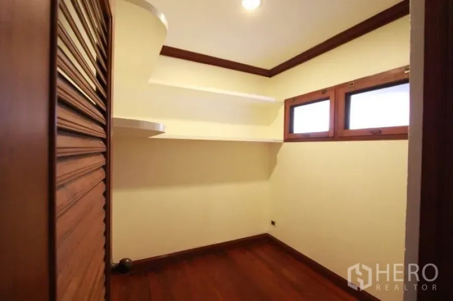 Detached House for rent in Prawet, Bangkok - Compact storage room with floating shelves, wooden louvered door and small high windows over hardwood floors.