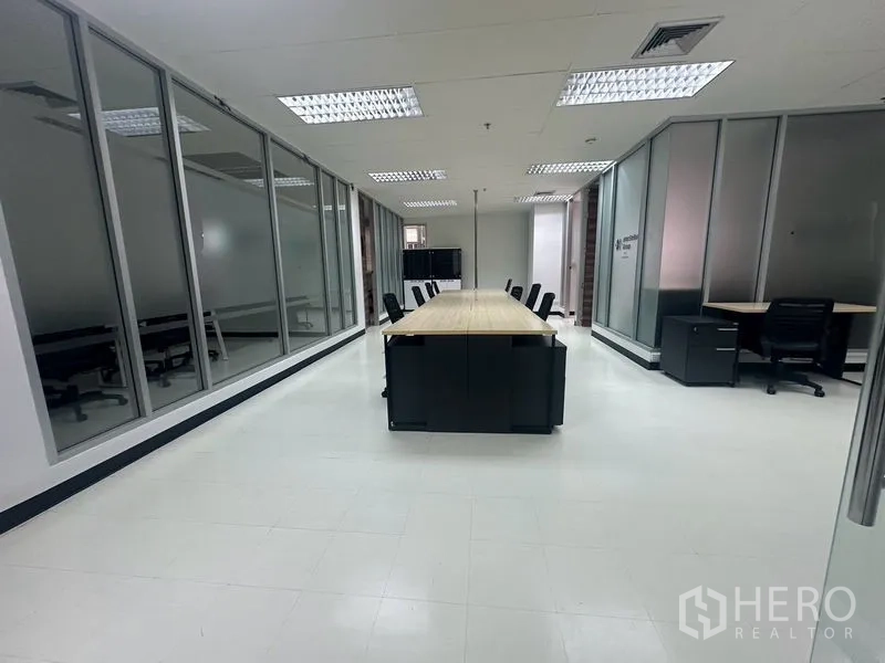 Office Space for rent - Open-plan office with a long shared desk, glass-partitioned rooms, bright ceiling lights, and tiled floor in Chatuchak.
