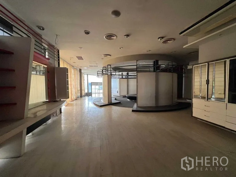 Retail Space for rent - Spacious retail showroom with circular display structure, built-in shelving, wood flooring and floor-to-ceiling windows.