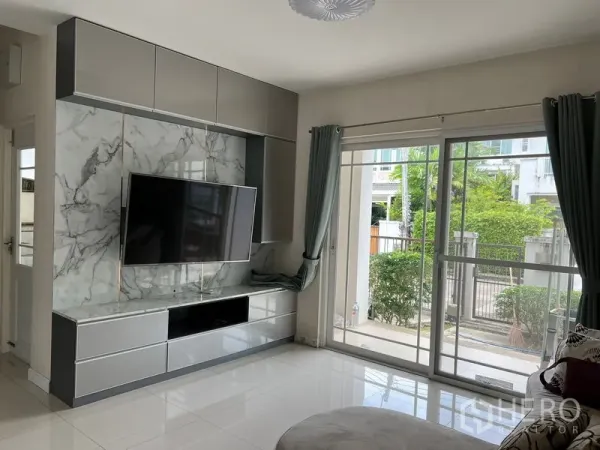 Detached House for rent in Bang Kapi, Bangkok - Living area with built-in TV cabinet and large windows with grey curtains.