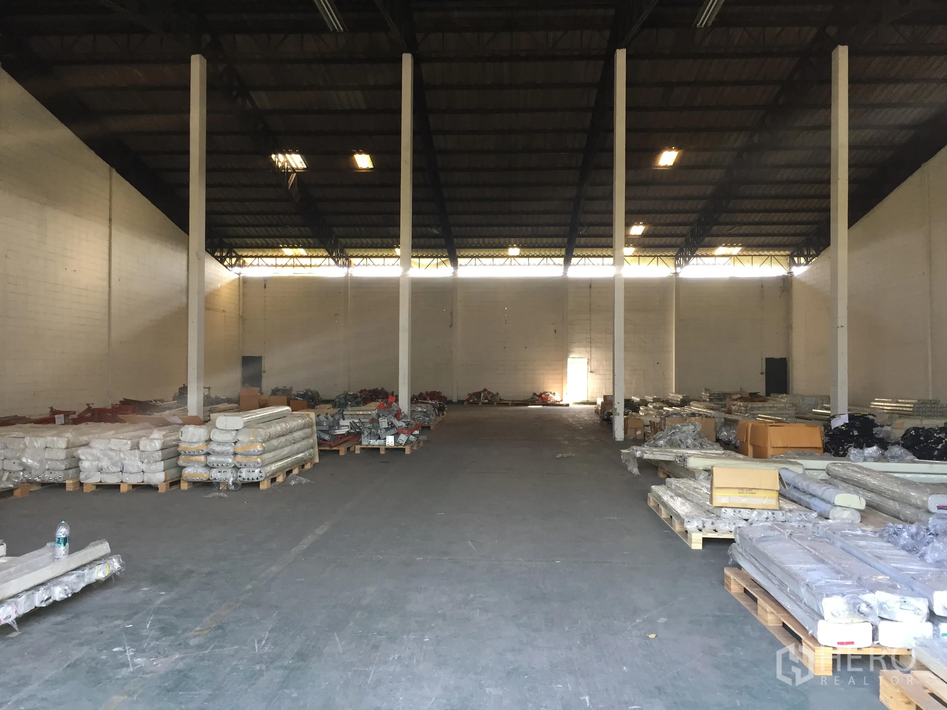 Factory for rent in Pathum Thani - Spacious factory interior with high steel roof, tall columns and stacked pallets on the floor.