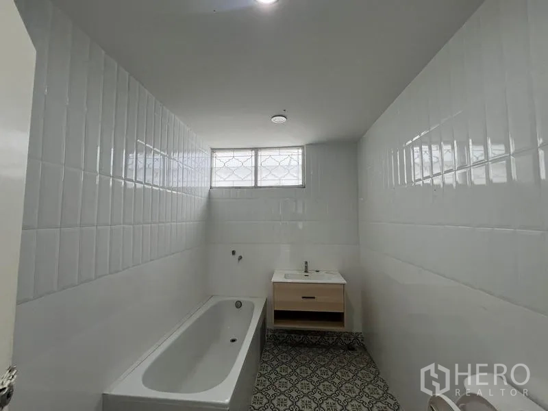 Home Office for rent in Watthana, Bangkok - Bathroom with bathtub, white wall tiles, and patterned floor tiles.