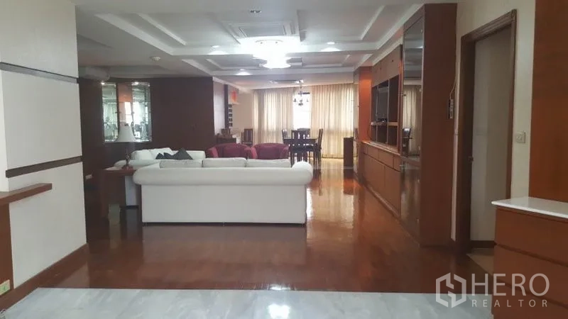 Condominium for rent in Khlong Toei, Bangkok - Wide living space with white sofa set, media cabinetry, and floor-to-ceiling curtains.